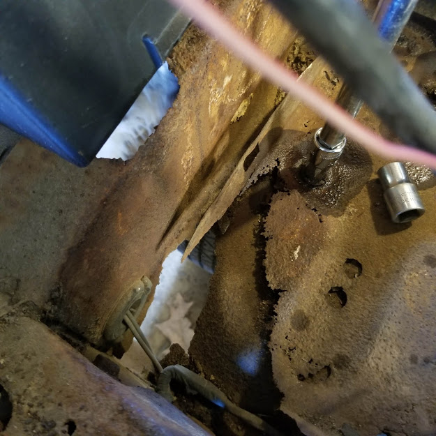 View of the battery compartment showing rusted, corroded metal and a socket wrench in the process of disassembly.